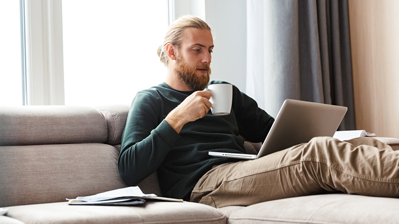 Person on sofa with laptop, holding a mug
