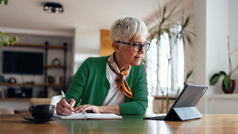 Person sitting at table with tablet device, pen and notepad