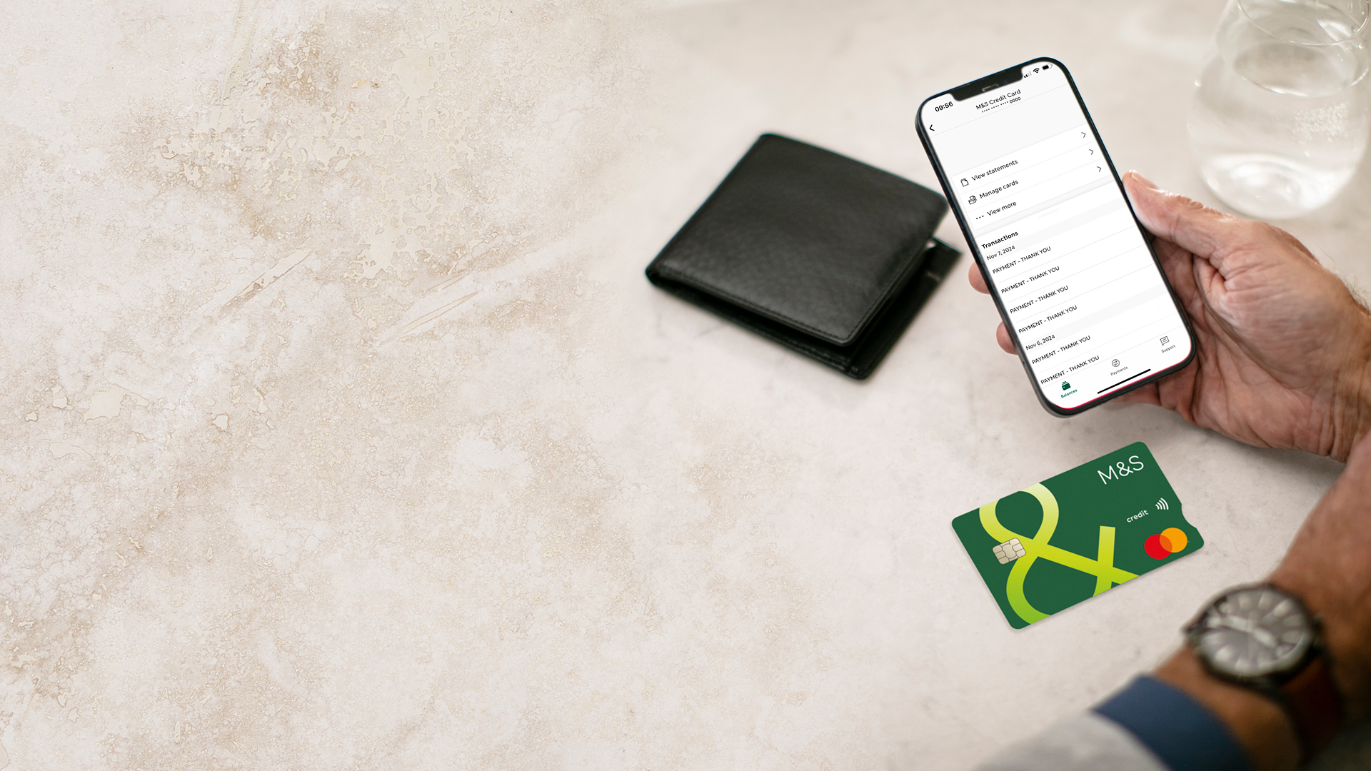 Using the M&S Banking App at a table with a wallet, an M&S Credit Card and a glass of water on it