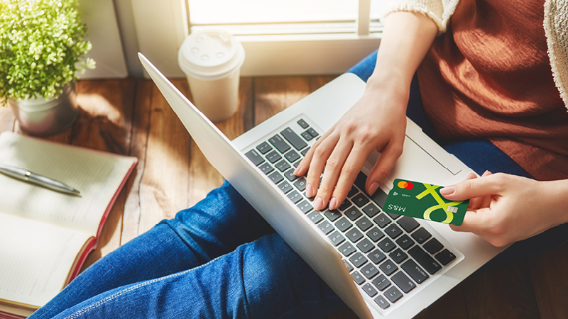 Person sat on floor with laptop holding Credit Card