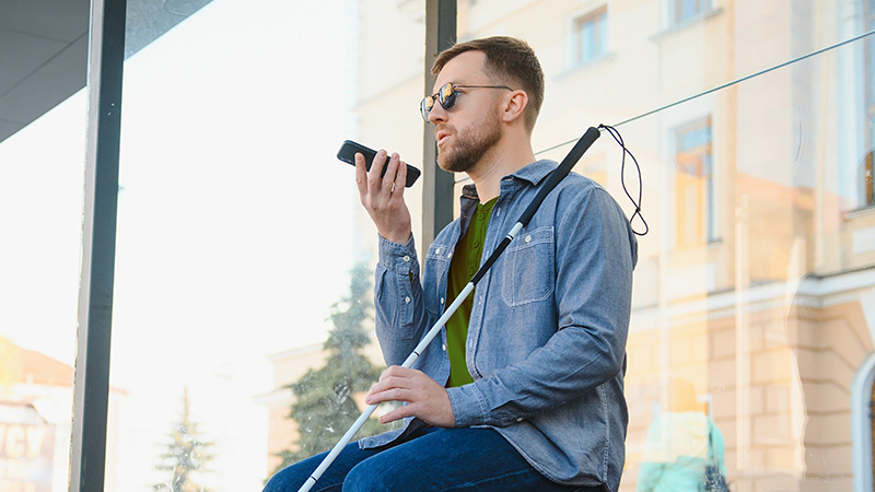 blind man sitting outside with phone and cane